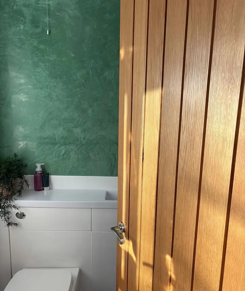 Green polished plaster cloakroom wall seen past an oak door